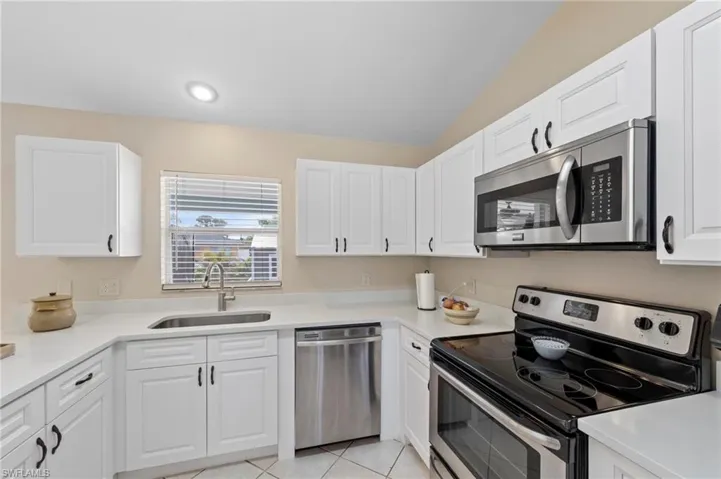 Kitchen featuring white cabinetry, light countertops, stainless steel appliances, and a window with blinds