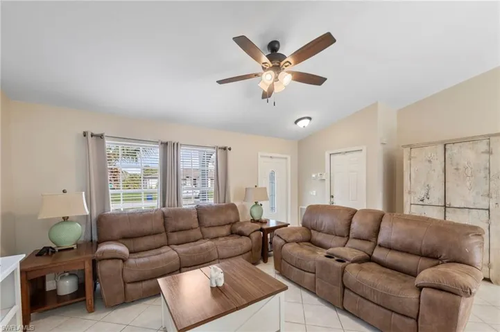 Vaulted ceiling living area featuring tile flooring, ceiling fan with integrated lighting, and multiple windows with blinds