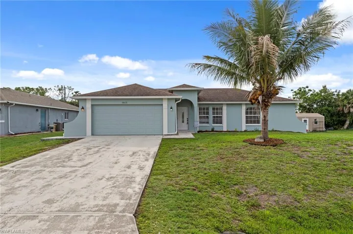 Light blue stucco exterior featuring a two-car garage, mature palm tree, and concrete driveway