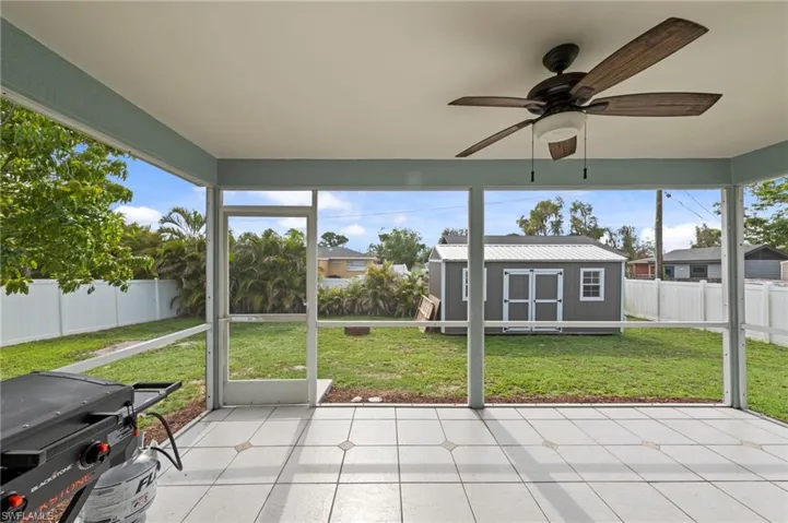 Screened patio featuring a ceiling fan with light fixture, tiled flooring, and a shed with a metal roof