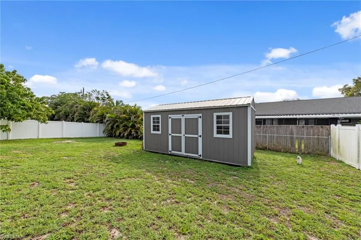 Spacious backyard featuring a gray storage shed with a metal roof, white trim, and windows