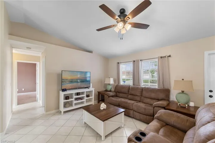 Spacious living area featuring vaulted ceilings, ceiling fan with light fixture, tile flooring, and multiple windows
