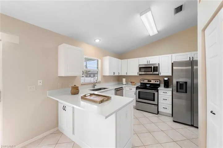 Kitchen with white shaker cabinetry, stainless steel appliances, light countertops, and tile flooring