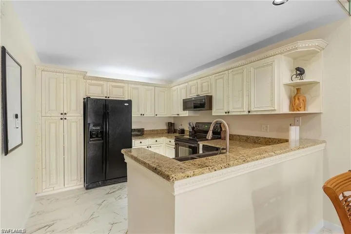 Kitchen with black appliances, cream cabinetry, a peninsula, and marble finish floor