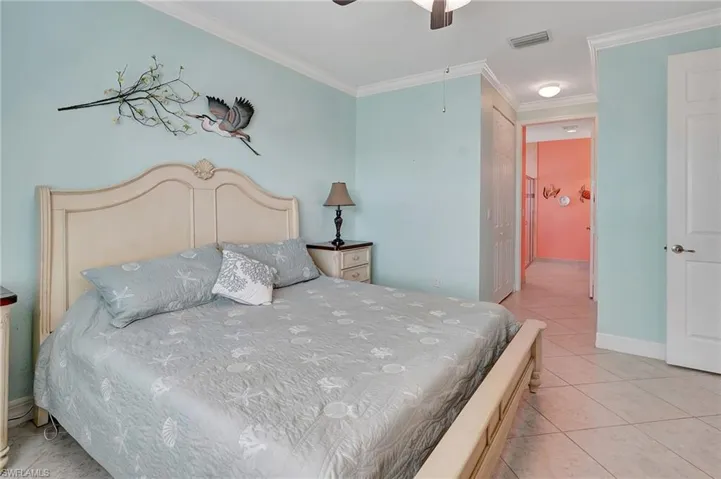 Bedroom featuring light tile patterned floors, ornamental molding, a closet, ensuite bathroom, and a ceiling fan