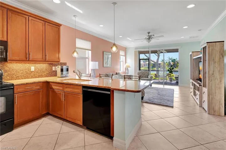 Kitchen featuring black appliances, a peninsula, a kitchen breakfast bar, light tile patterned flooring, and ornamental molding