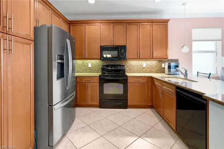 Kitchen featuring open floor plan, light tile patterned floors, black appliances, tasteful backsplash, and brown cabinets