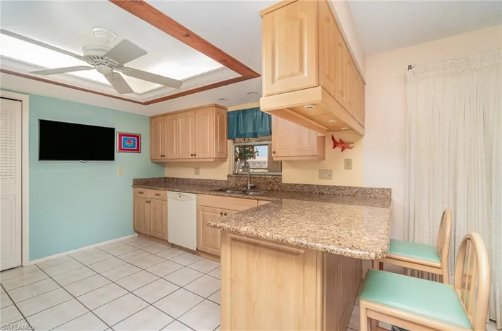 Kitchen with light stone countertops, ceiling fan, dishwasher, light tile floors, and sink