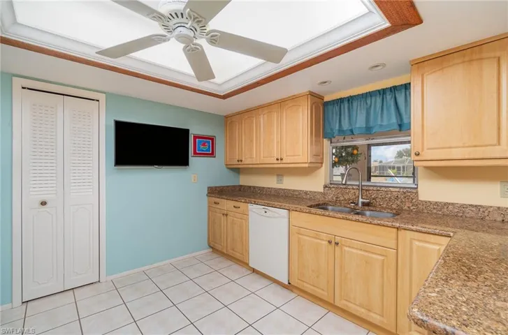 Kitchen with sink, dishwasher, light brown cabinetry, and ceiling fan