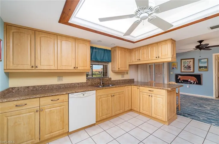 Kitchen featuring white dishwasher, dark stone countertops, light carpet, sink, and ceiling fan