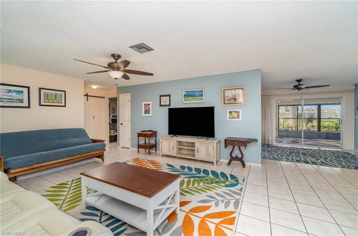 Living room featuring a barn door, a textured ceiling, light tile flooring, and ceiling fan