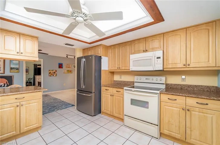 Kitchen featuring ceiling fan, a tray ceiling, white appliances, and light tile floors