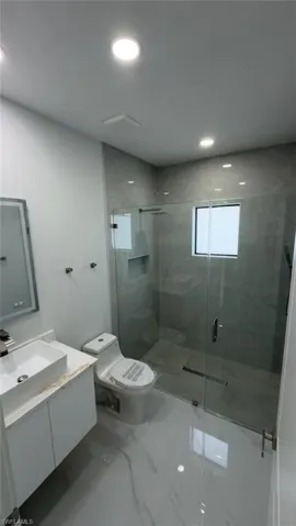 Spacious bathroom featuring a glass-enclosed shower, white vanity with vessel sink, modern toilet, and large format polished floor tiles