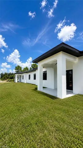 Contemporary exterior with white stucco finish, dark framed windows, covered patio, and extensive green lawn