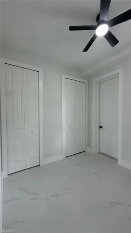 White walls, light-toned flooring with subtle veining, white bi-fold doors, and a ceiling fan with integrated lighting