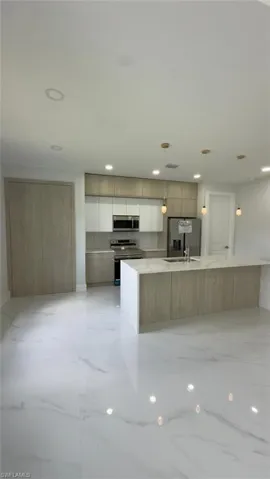 White tile flooring throughout, featuring a kitchen island with seating, stainless steel appliances, and wood-finish cabinetry