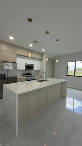 Kitchen featuring a waterfall island with stone countertop, stainless steel appliances, wood-finish cabinetry, recessed lighting, and pendant lighting