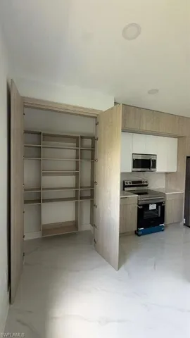 Built-in storage with adjustable shelving, integrated kitchen cabinetry, stainless steel microwave, electric range, and light-toned flooring