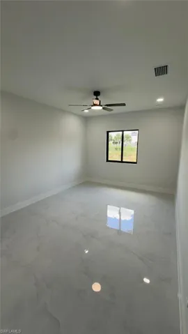 Polished light-toned flooring, recessed lighting, ceiling fan with integrated light, and large window with dark frame