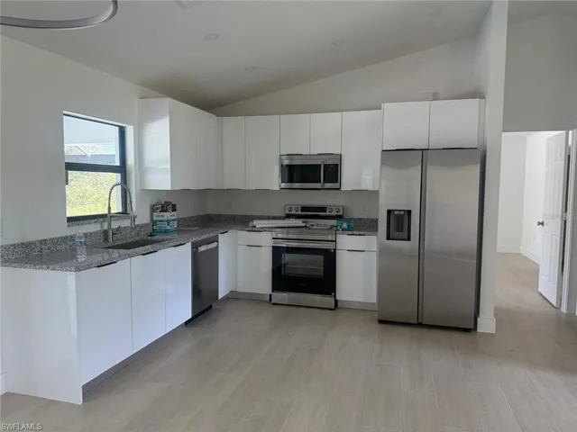 Kitchen featuring stainless steel appliances, white cabinets, dark stone counters, modern cabinets, and vaulted ceiling