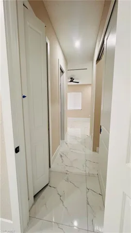 Hallway featuring large format white tile flooring with grey veining, white trim, and recessed lighting