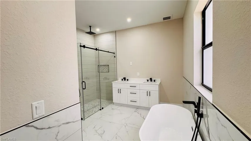 Bathroom featuring a freestanding soaking tub, dual vanity with white cabinetry, walk-in shower with glass enclosure, rain shower head, and floor-to-ceiling tile in shower