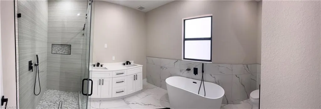 Bathroom featuring a freestanding soaking tub, a frameless glass shower enclosure with pebble floor, a dual vanity with white cabinetry, and matte black fixtures throughout