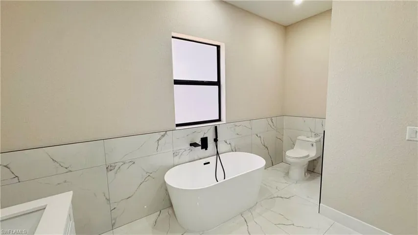 Bathroom featuring a freestanding tub with a matte black floor-mounted faucet, large format tile flooring, and matching wainscoting