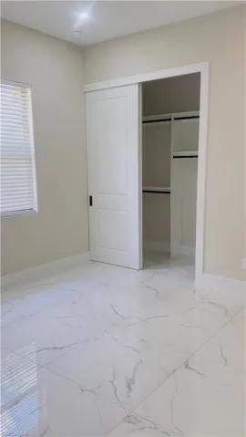 Spacious room featuring large format white tile flooring with grey veining, a white sliding barn door, and a built-in closet system with shelving and hanging rods