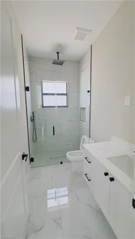 Contemporary bathroom featuring a spacious glass-enclosed shower with a rainfall showerhead, large format white tile flooring, and a white vanity with an integrated sink and dark hardware
