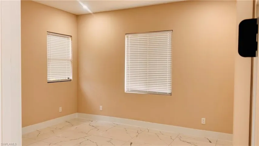 Room with two windows featuring white blinds, light beige walls, and light-colored tile flooring with dark veining