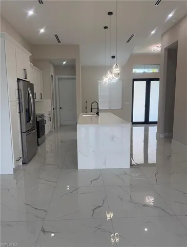 Open-concept kitchen featuring an expansive island with waterfall-edge countertop, stainless steel appliances, white cabinetry with black hardware, and large format polished tile flooring