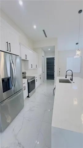 Gourmet kitchen featuring stainless steel appliances, crisp white cabinetry with black hardware, white stone countertops, and polished tile flooring