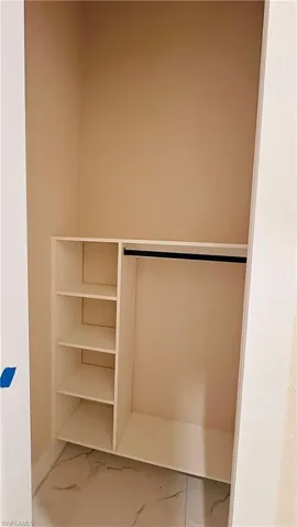 Built-in closet system featuring shelving and a hanging rod, set against light neutral walls and marble-look floor tile