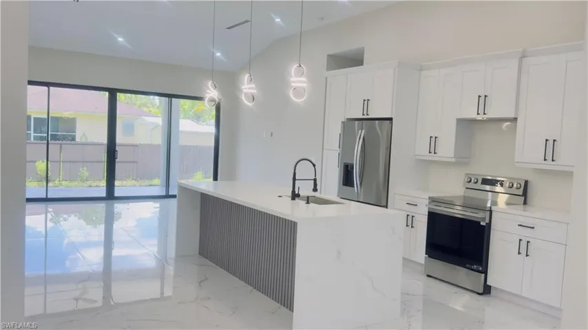 Modern kitchen featuring a waterfall island with fluted paneling and pendant lighting, white shaker cabinetry, stainless steel appliances, and large format polished tile flooring