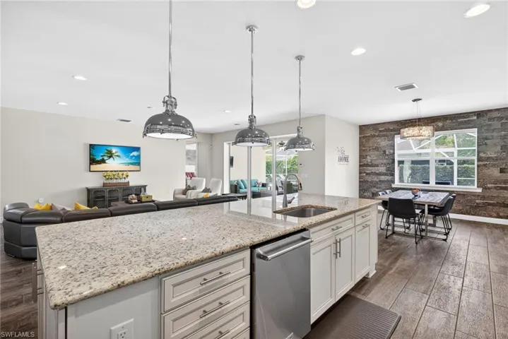Kitchen featuring dark wood finished floors, open floor plan, a kitchen island with sink, light stone counters, and dishwasher