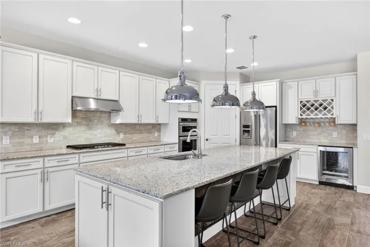 Kitchen with dark wood-style floors, a breakfast bar, wine cooler, stainless steel appliances, and light stone countertops