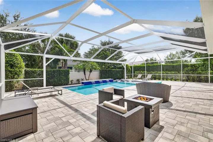View of pool featuring glass enclosure, patio surround, a sunroom, and a fire pit