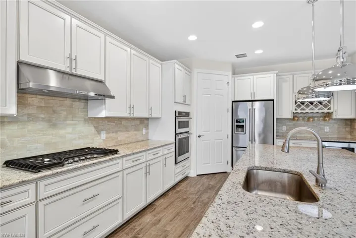 Kitchen featuring pendant lighting, white cabinetry, stainless steel appliances, dark wood-style floors, and light stone counters