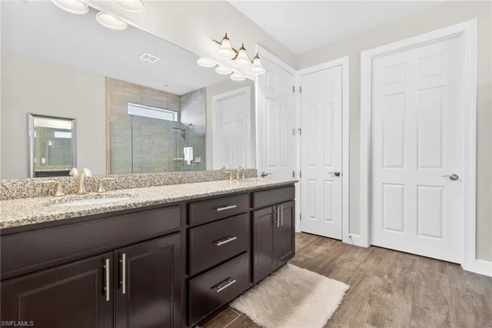 Bathroom featuring a shower stall, double vanity, and dark wood-style floors