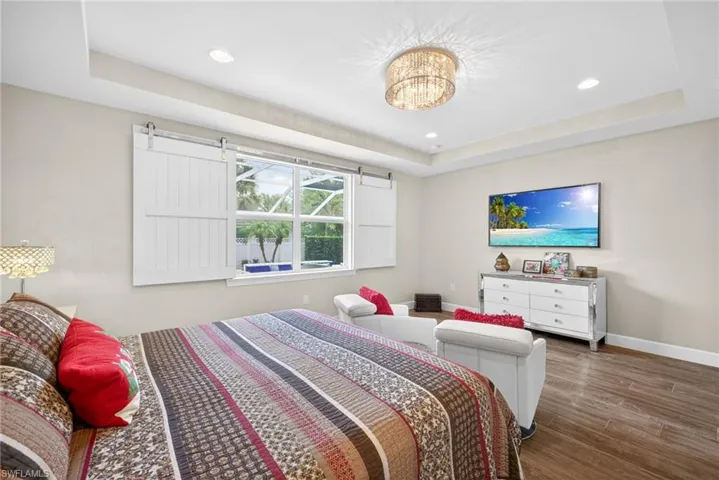 Bedroom with a raised ceiling, dark wood-style flooring, and suspended lighting
