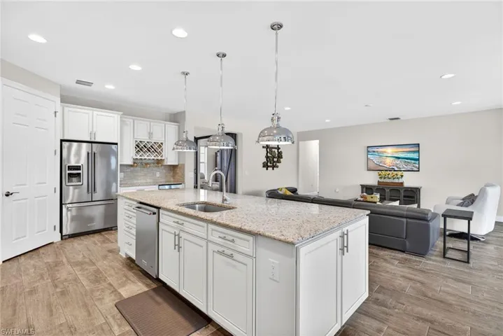 Kitchen featuring white cabinetry, stainless steel appliances, light stone counters, light wood-type flooring, and open floor plan