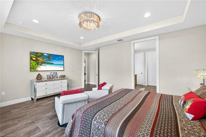 Bedroom with a tray ceiling, dark wood-style flooring, and recessed lighting