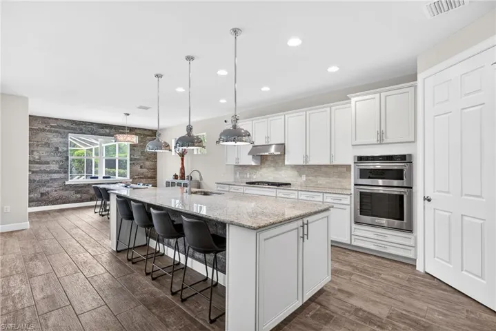 Kitchen featuring a breakfast bar area, stainless steel double oven, a center island with sink, white cabinetry, and light stone countertops