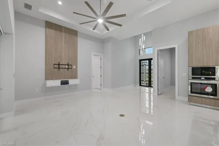 Unfurnished room featuring a tray ceiling, ceiling fan, light marble finish floors, and a high ceiling