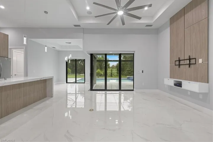 Unfurnished living room with a tray ceiling, ceiling fan, and light marble finish floors