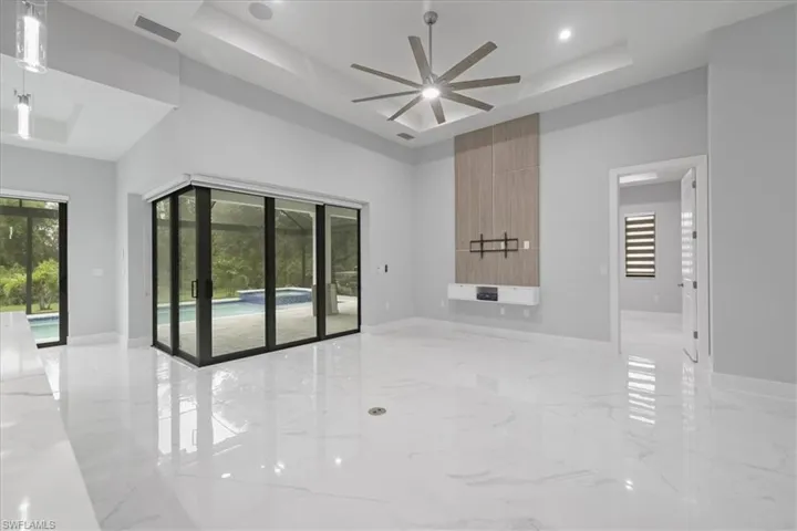 Unfurnished room featuring a tray ceiling, ceiling fan, a towering ceiling, light marble finish flooring, and recessed lighting