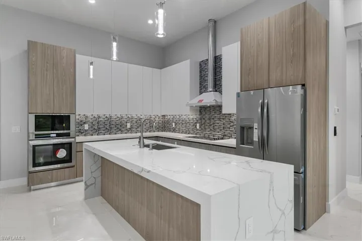 Kitchen featuring stainless steel fridge, modern cabinets, backsplash, cooktop, and light marble finish floors