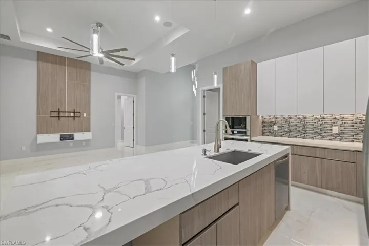 Kitchen featuring modern cabinets, a tray ceiling, ceiling fan, light stone counters, and recessed lighting