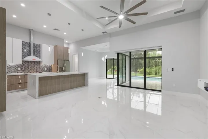 Kitchen featuring modern cabinets, stainless steel fridge, wall chimney exhaust hood, backsplash, and ceiling fan